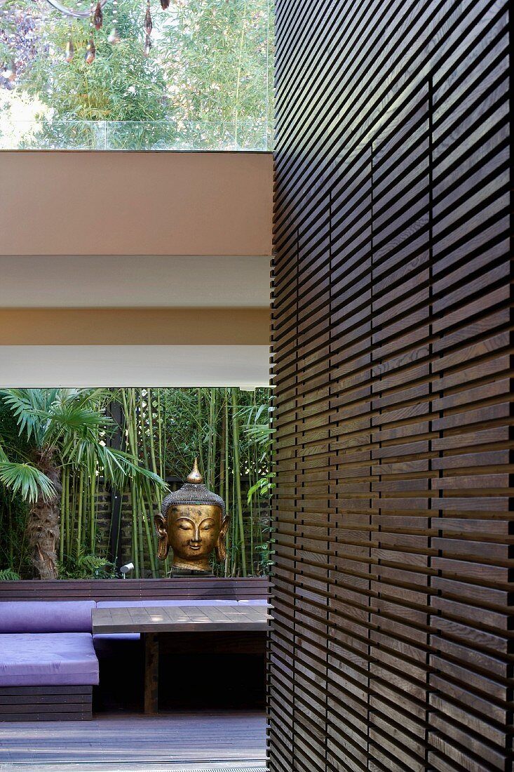 Wood-clad wall with integrated fitted cupboard and head of Buddha on windowsill