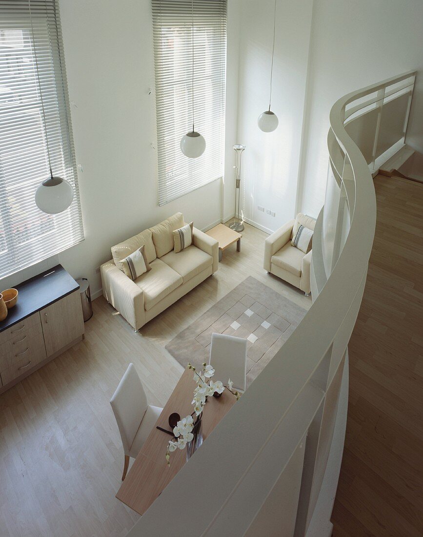 Blick von geschwungener Galerie auf offenen Wohnraum mit hellem modernem Sofa und Polstermöbel auf Parkett