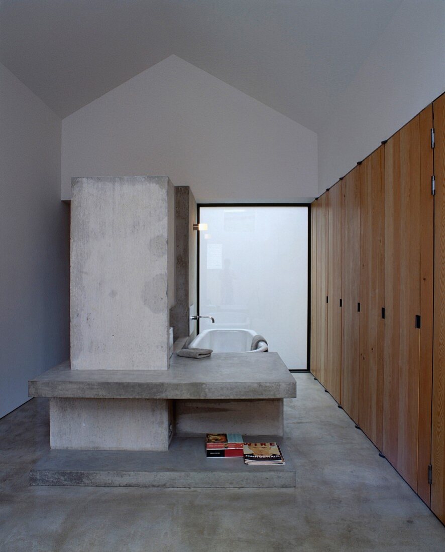 Designer bathroom with concrete partition and shelf in front of bathtub
