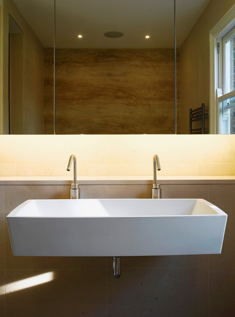 Grosses Waschbecken mit zwei Designerarmaturen unter Spiegelschrank mit indirekter Beleuchtung