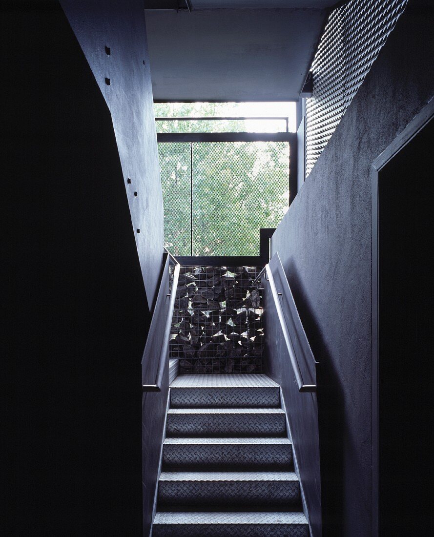 Schmaler Treppenaufgang mit Stufen und Geländer aus Metall und Wand aus Gabione
