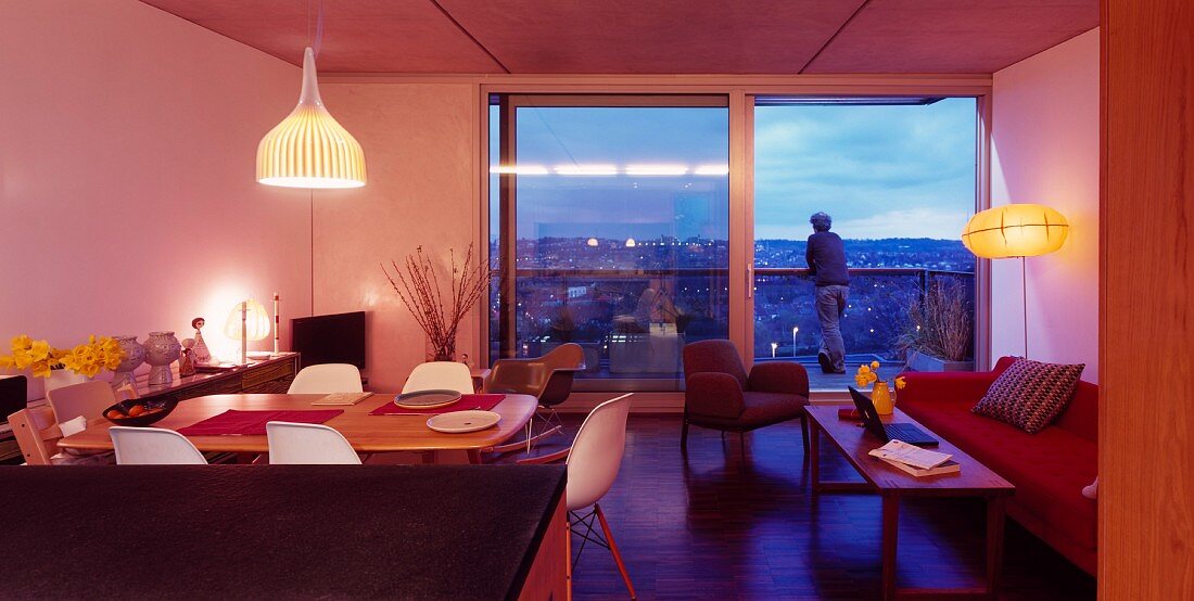 Modern, open-plan living room with dining area and floor to ceiling terrace windows in the evening