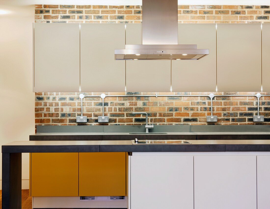 Modern kitchen units with white wall-mounted cupboards and indirect lighting on a brick wall