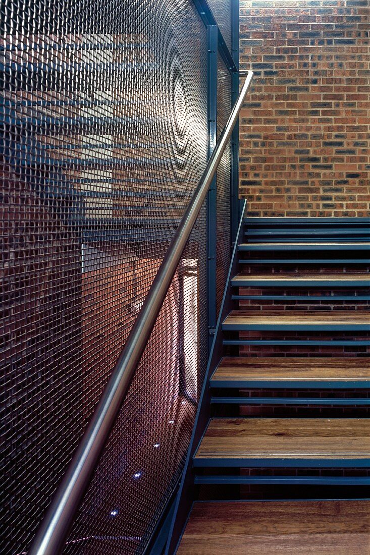 Treppenaufgang aus Holz und Metall mit transparenter Gitterrostwand in Fabrikhalle