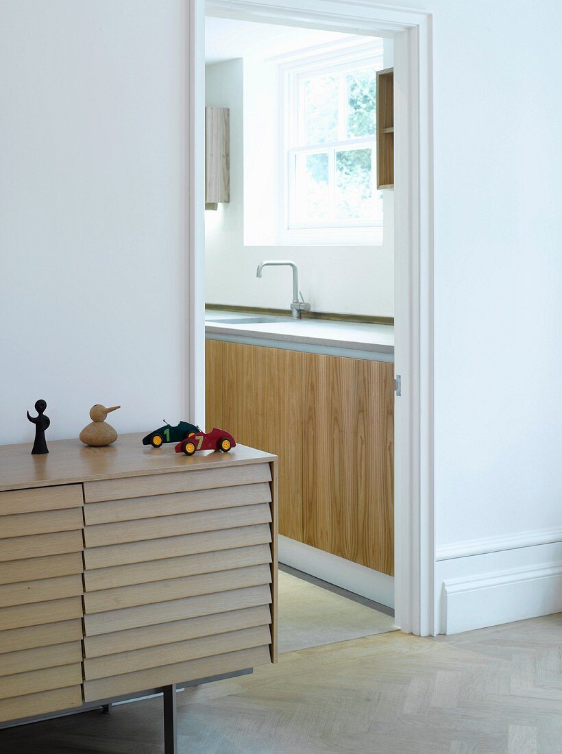 Modernes Sideboard mit geschuppter Holzstabfront neben offener Küchentür