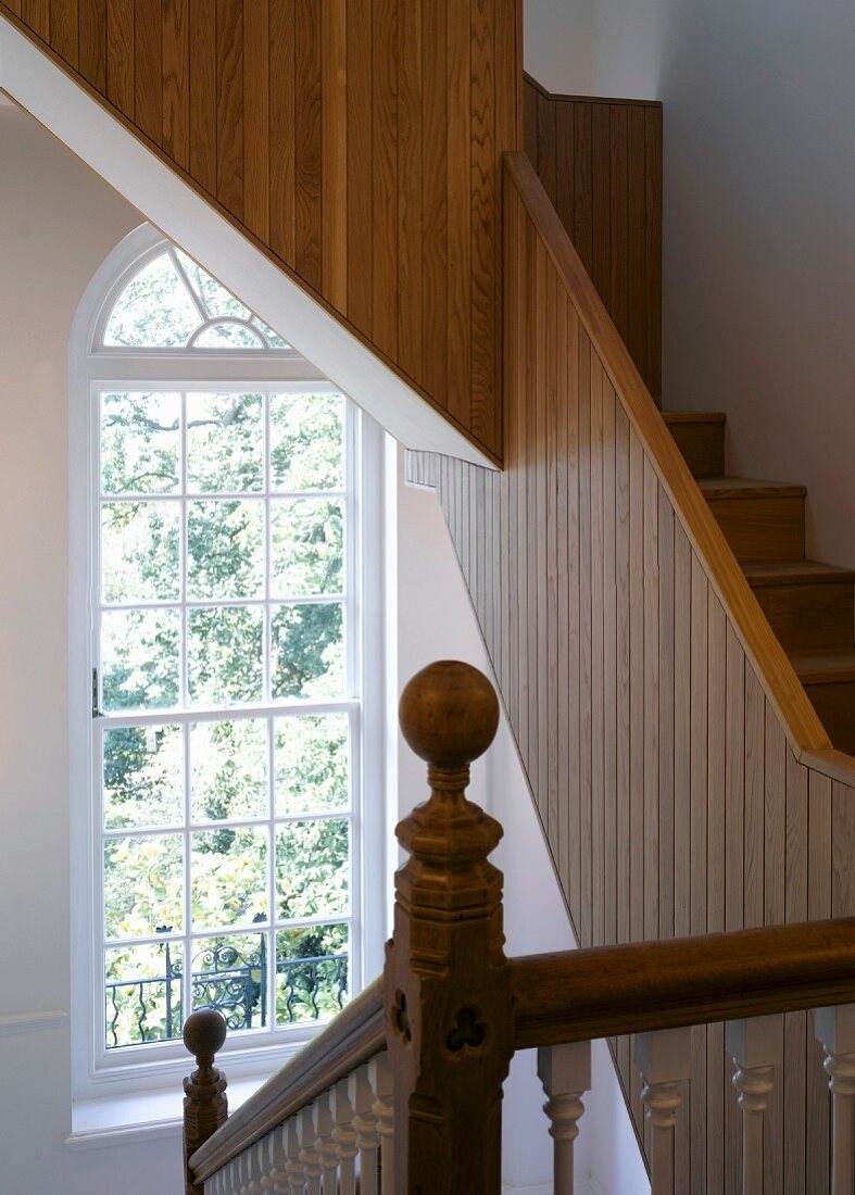 Traditionelles Treppenhaus mit Rundbogenfenster und moderne Holztreppe mit geschlossenem Geländer