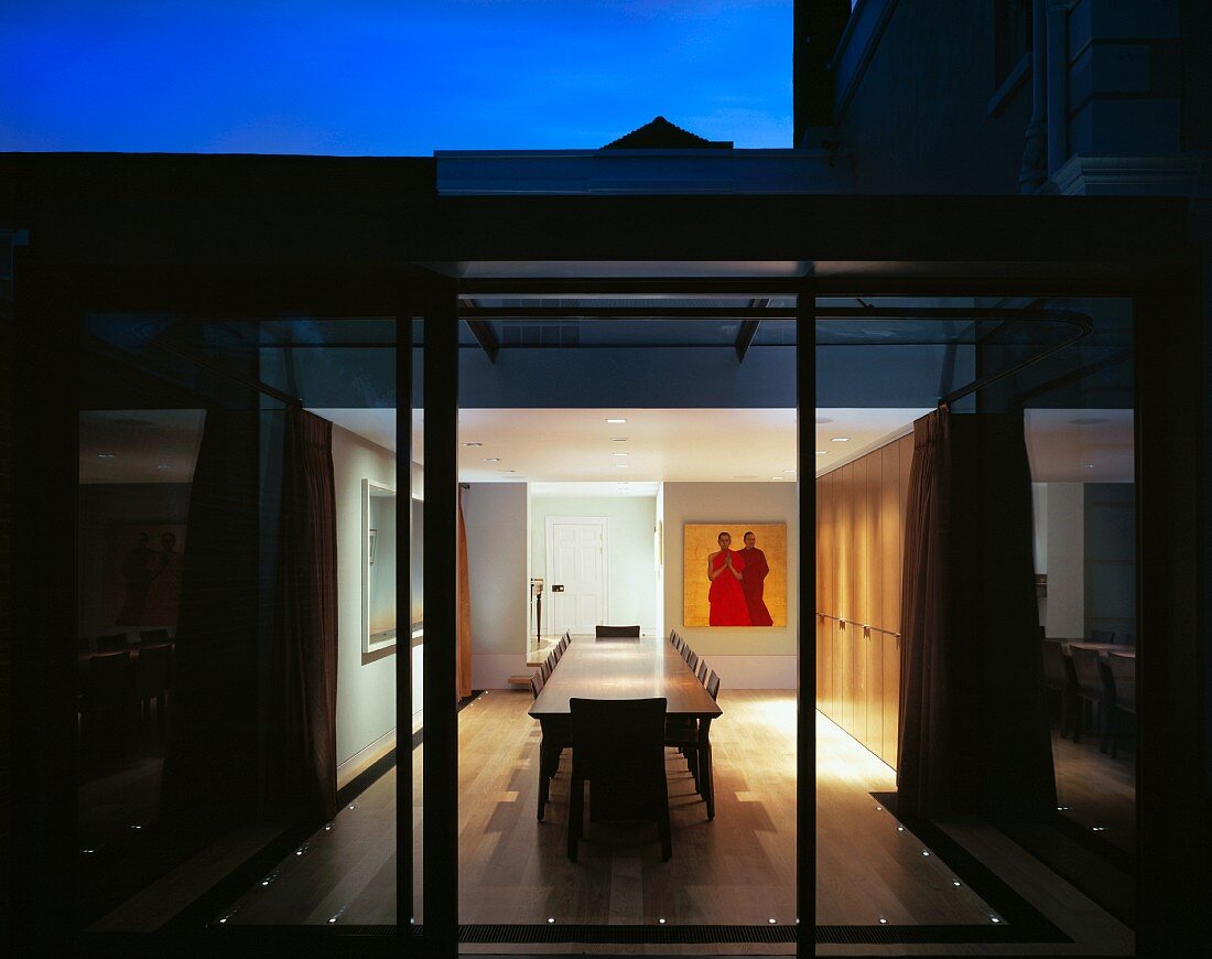 View through terrace window into illuminated interior with dining area in contemporary house