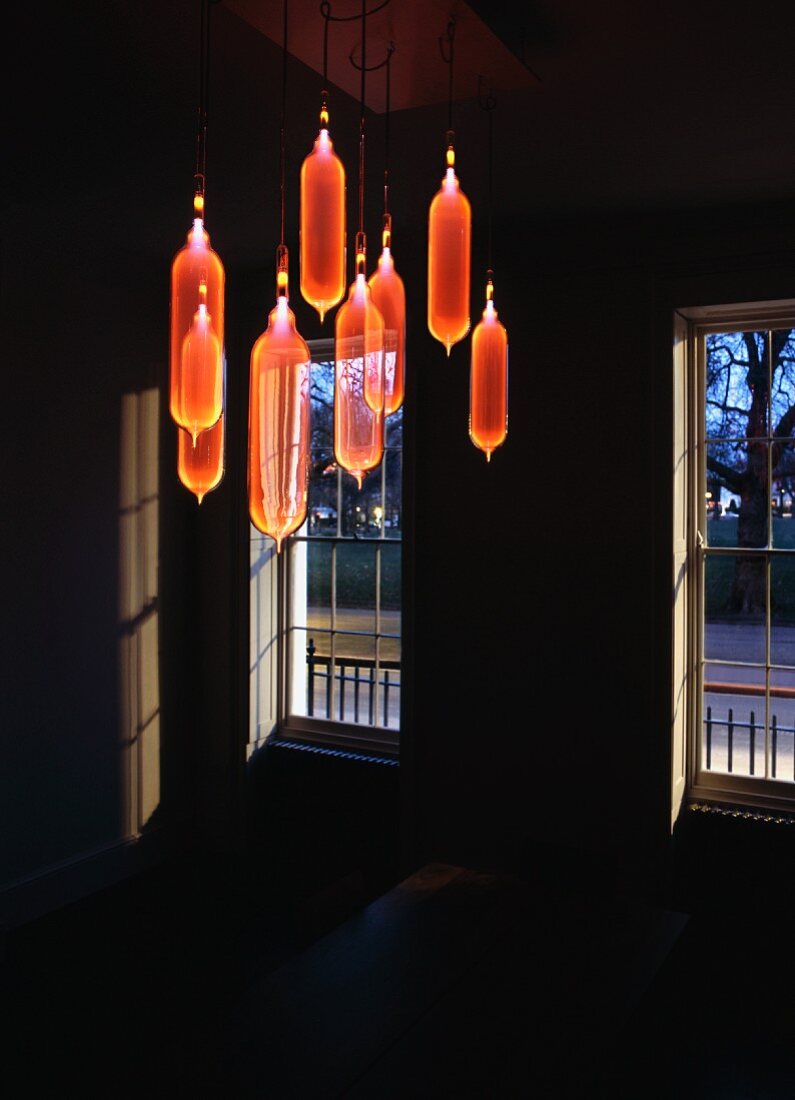 Lichtinstallation - von Decke hängende orange Glasballons im dunklen Raum
