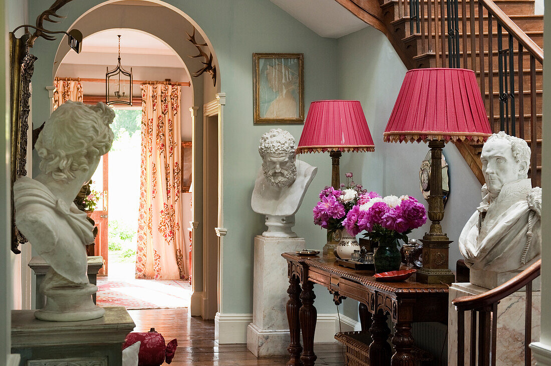 Hallway with marble busts, antique table and pink lampshades