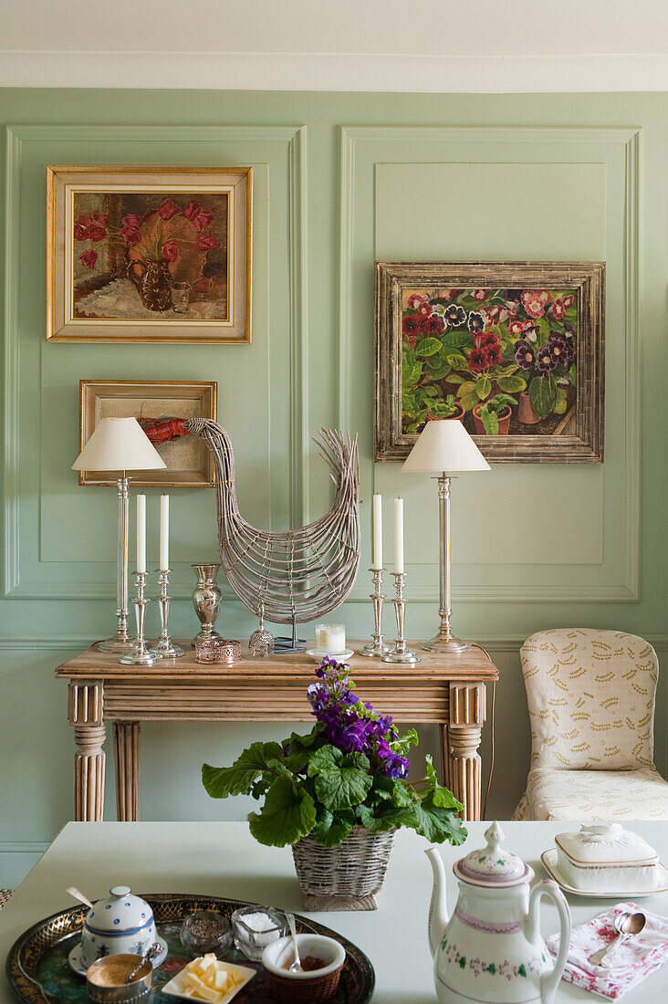 Console with candlesticks and table lamps, painting on green wall in living room