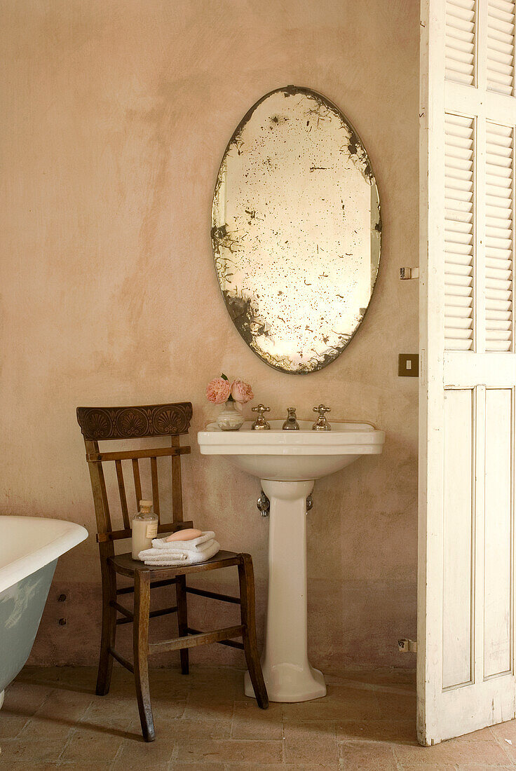 Holzstuhl und antiker, ovaler Spiegel im Vintage-Badezimmer