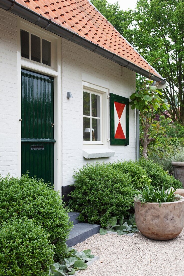 Entrance area of white brick house with dark green front door and graphic patterns on shutters