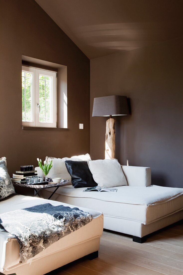 Elegant, white chaise longue below window in attic room painted dark brown