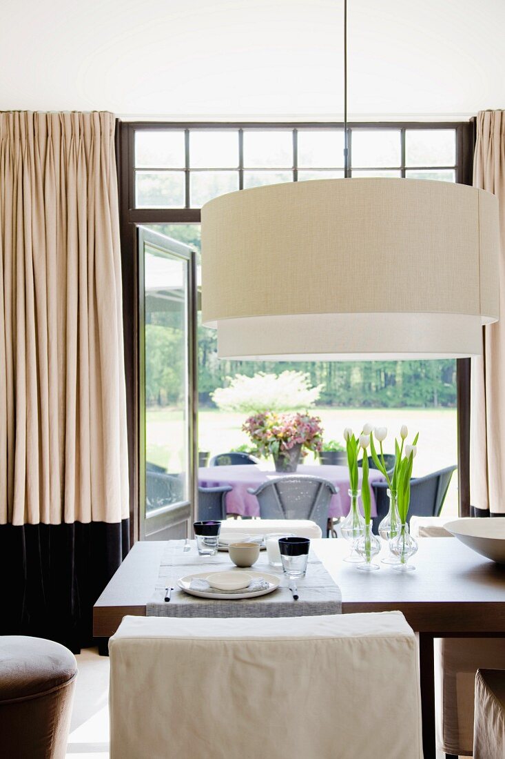 Large designer pendant lamp with white lampshade above set table in front of open terrace doors