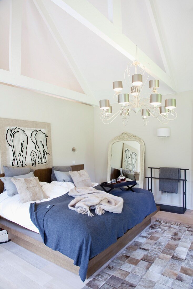 Double bed below chandelier with metal lampshades and patchwork fur rug