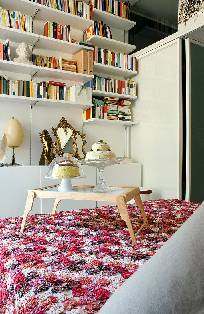 Modernes Schlafzimmer mit Wandregal, floraler Tagesdecke und kleinem Holztisch mit Gebäck