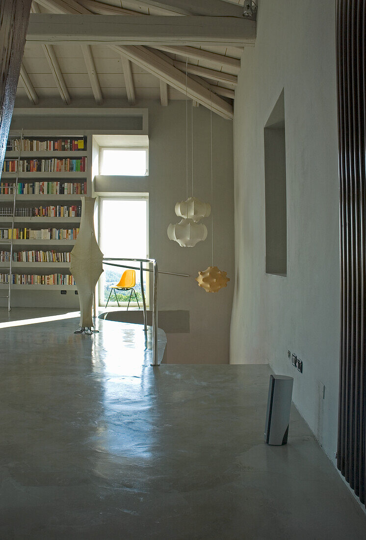 Puristically furnished living room with bookshelf, modern lamps and concrete floor