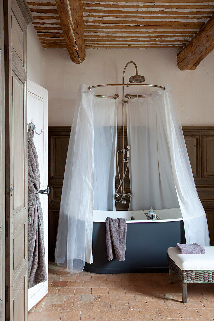 Freestanding bathtub with shower curtain in rustic bathroom with terracotta tiles