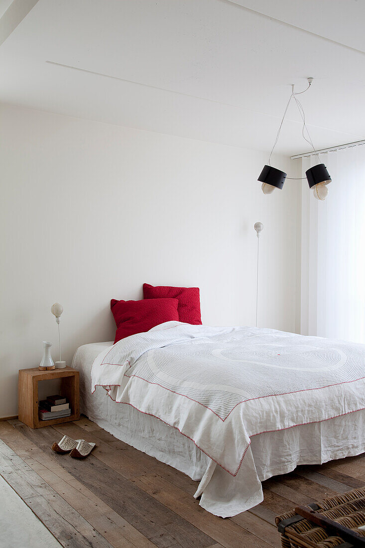 Minimalistisch gestaltetes Schlafzimmer mit weißer Bettwäsche und rotem Kissen