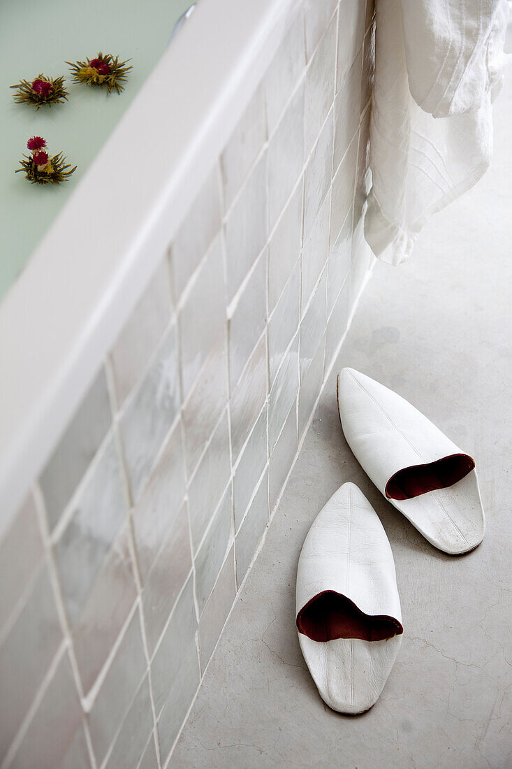 White Moroccan babouche next to tiled bathtub