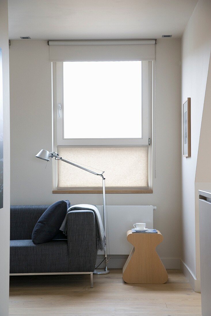 Ausschnitt einer Sitzecke im skandinavischen Designerstil mit Beistellhocker und Tolomeo Stehlampe vor Fenster mit Stoffrollo