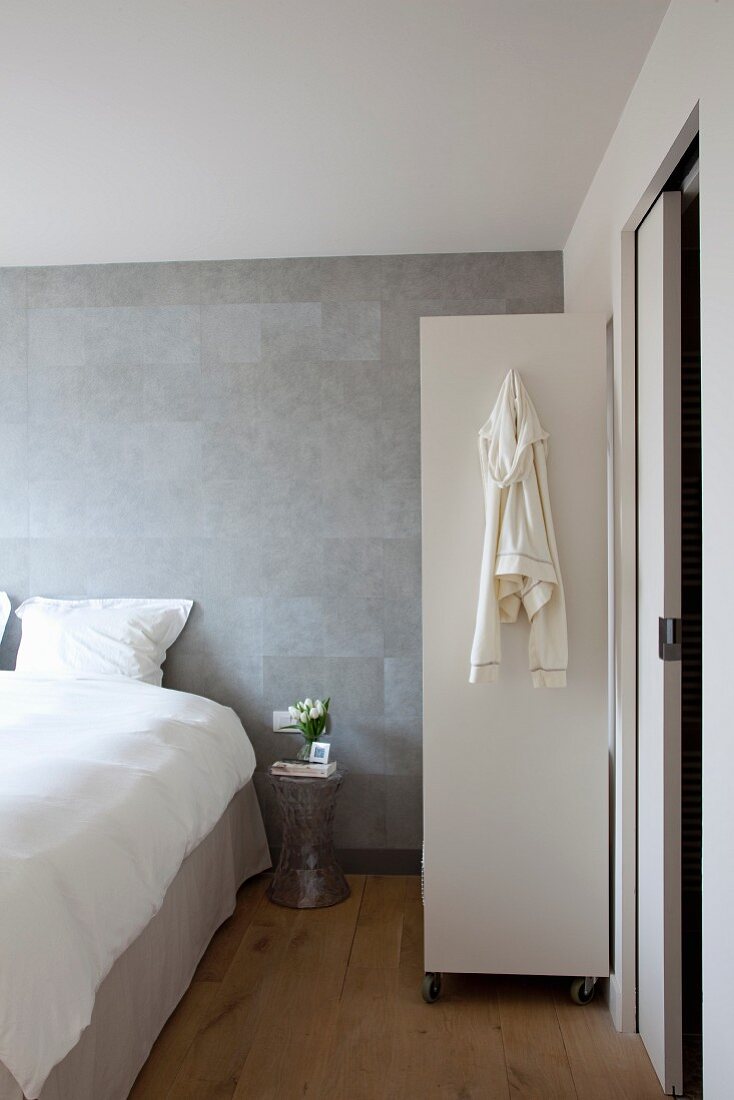 Schlafzimmer im skandinavischen Designerstil mit subtil changierender, grauer Wandgestaltung, Roll-Regal und Schiebetür zum Bad Ensuite
