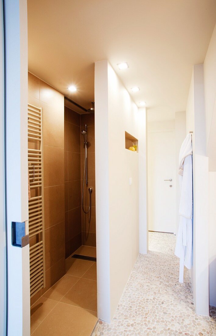 Caramel tiles in narrow shower cubicle and pebble mosaic floor in corridor