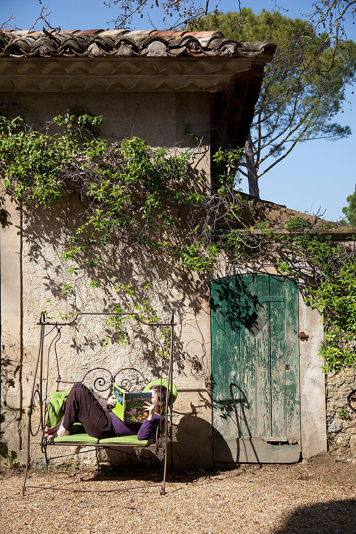 Boy lying on rocking bench in front of old stone wall