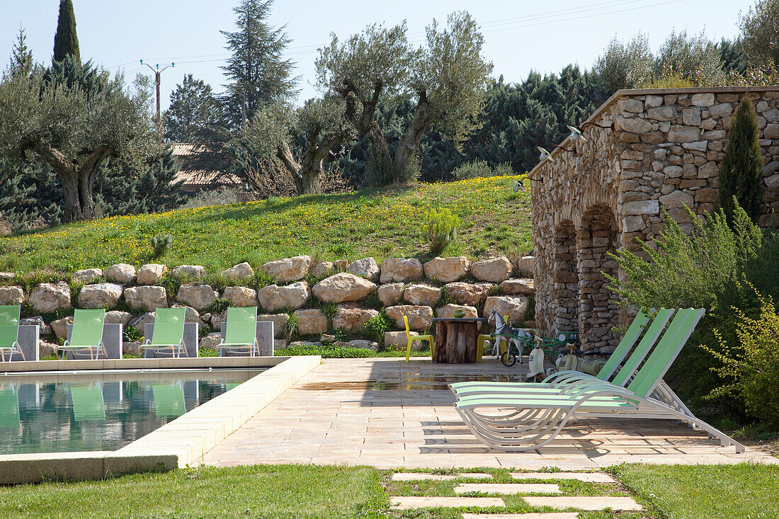 Pool area with sun loungers and stone wall in a Mediterranean garden landscape