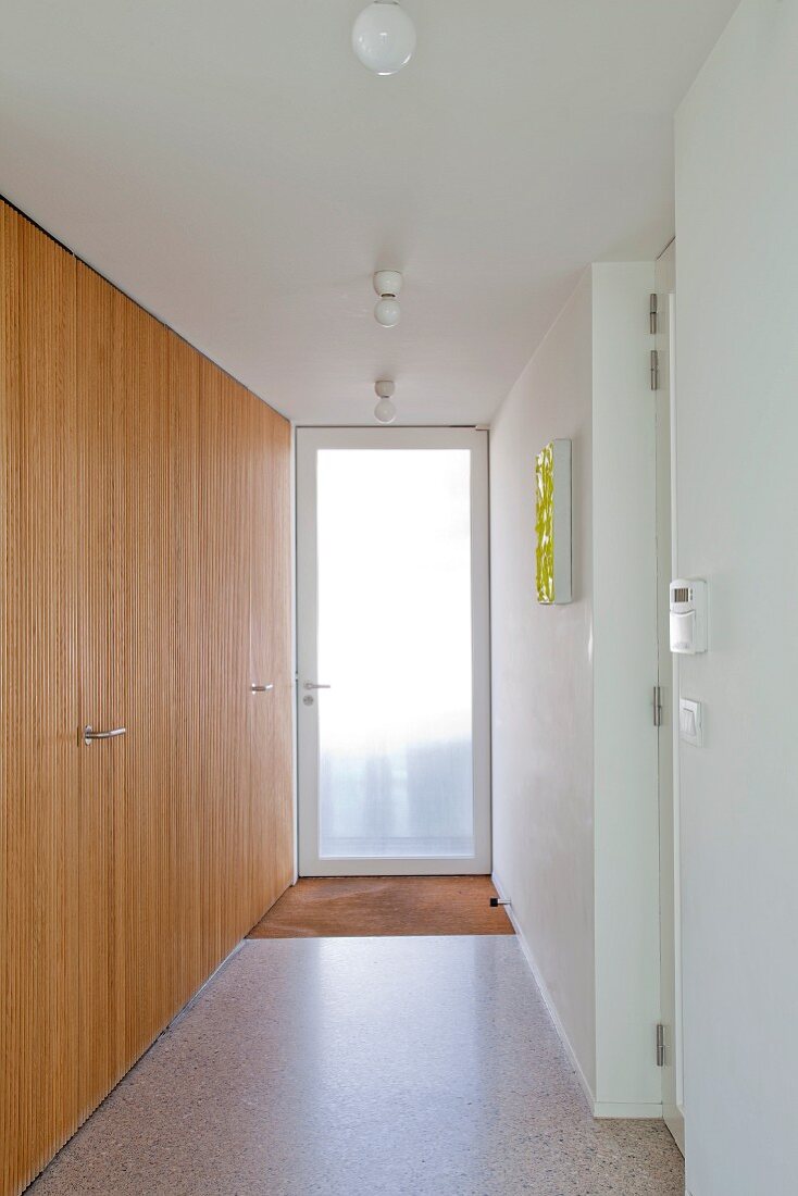 Glass terrace door at end of corridor and modern, wooden fitted cupboards