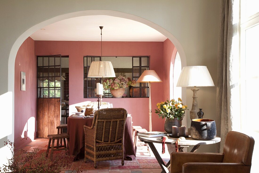 View through wide arched doorway of dining table, wicker chairs and walls painted dusky pink