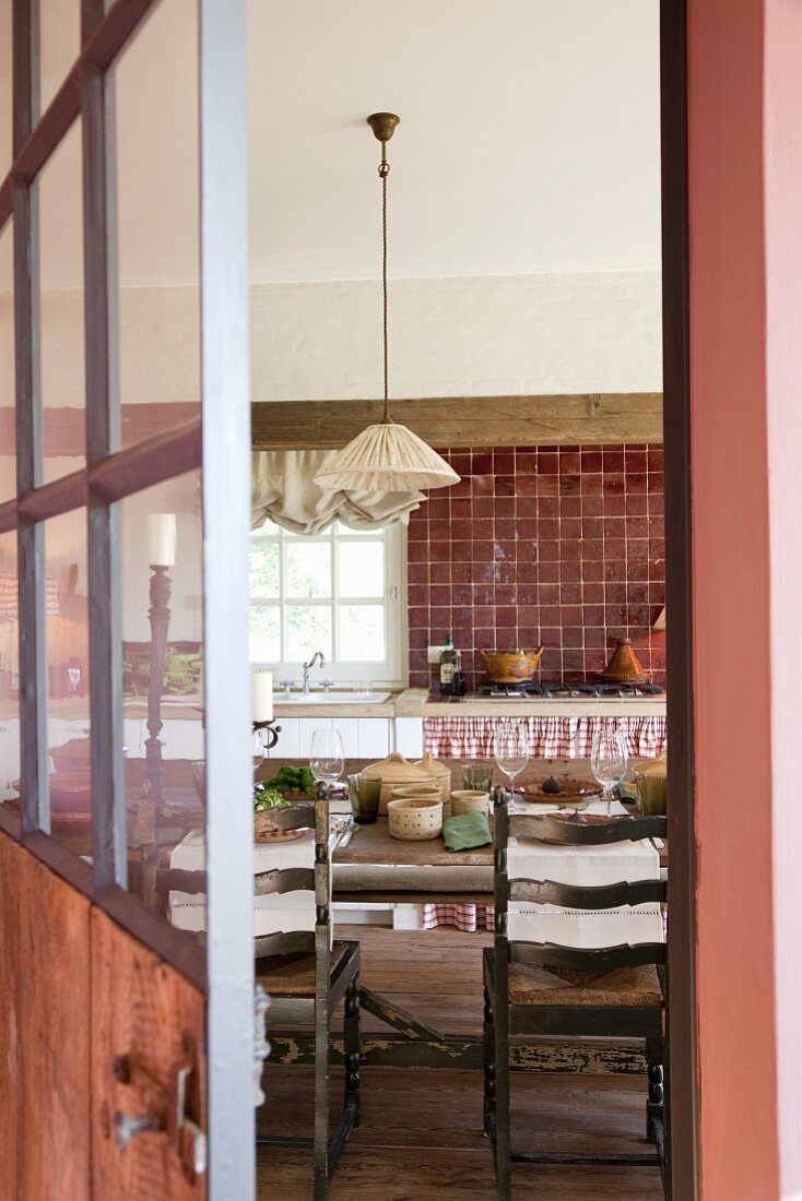 View through open door into rustic kitchen with dining area and dusky pink accents