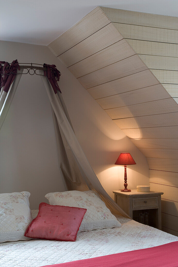 Schlafbereich unter Dachschräge mit Nachttisch und Tischlampe