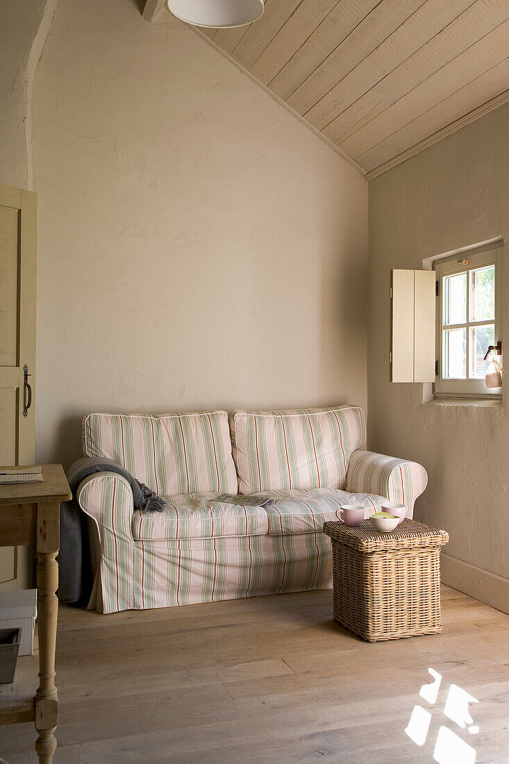 Hell gestreiftes Sofa und Rattankorb in hellem Landhausstil-Wohnzimmer im Dachgeschoss