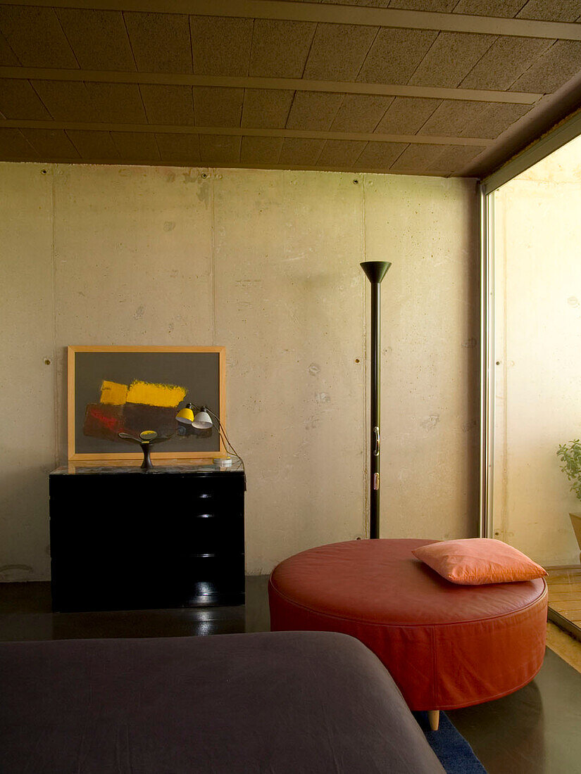 Minimalist room with concrete walls, black chest of drawers, black floor lamp and round ottoman