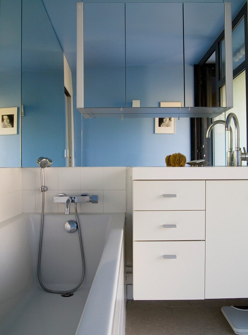 Modernes Bad mit Badewanne neben weißem Waschtisch vor grossflächigem Spiegel an Wand