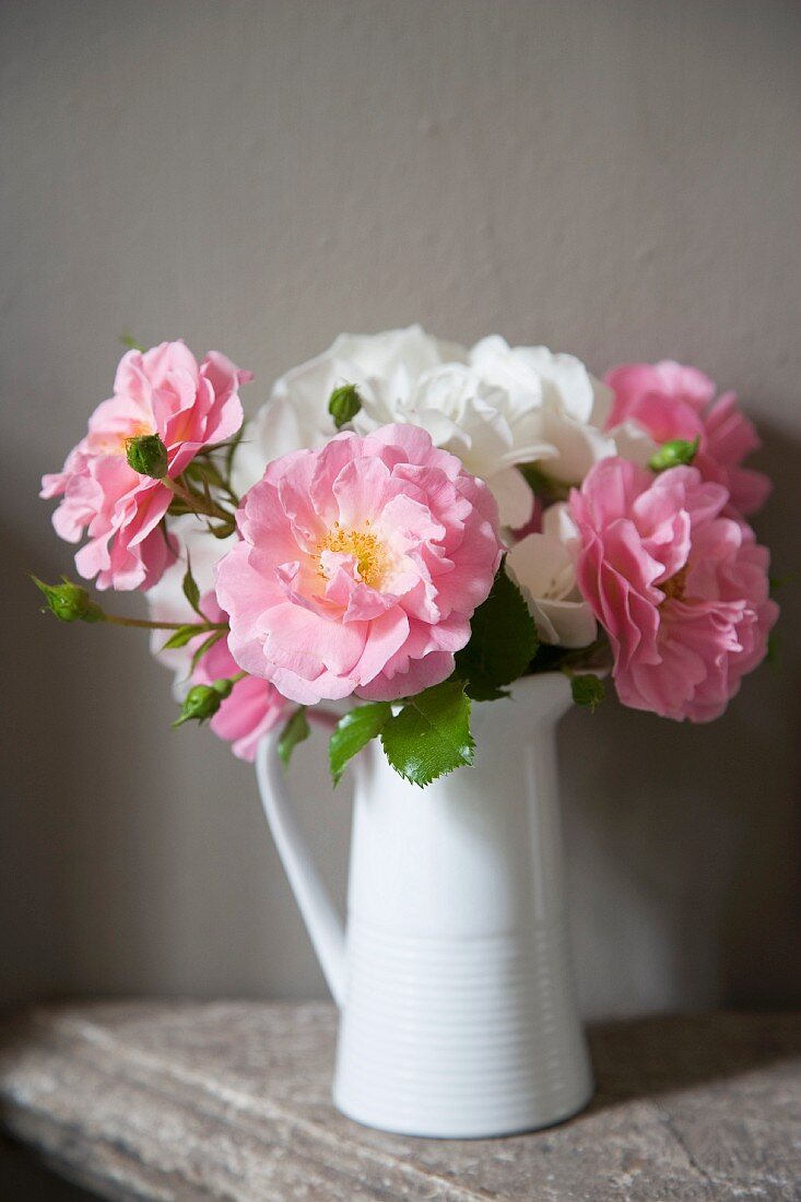 Bouquet of white and pink roses in vintage china jug against grey wall