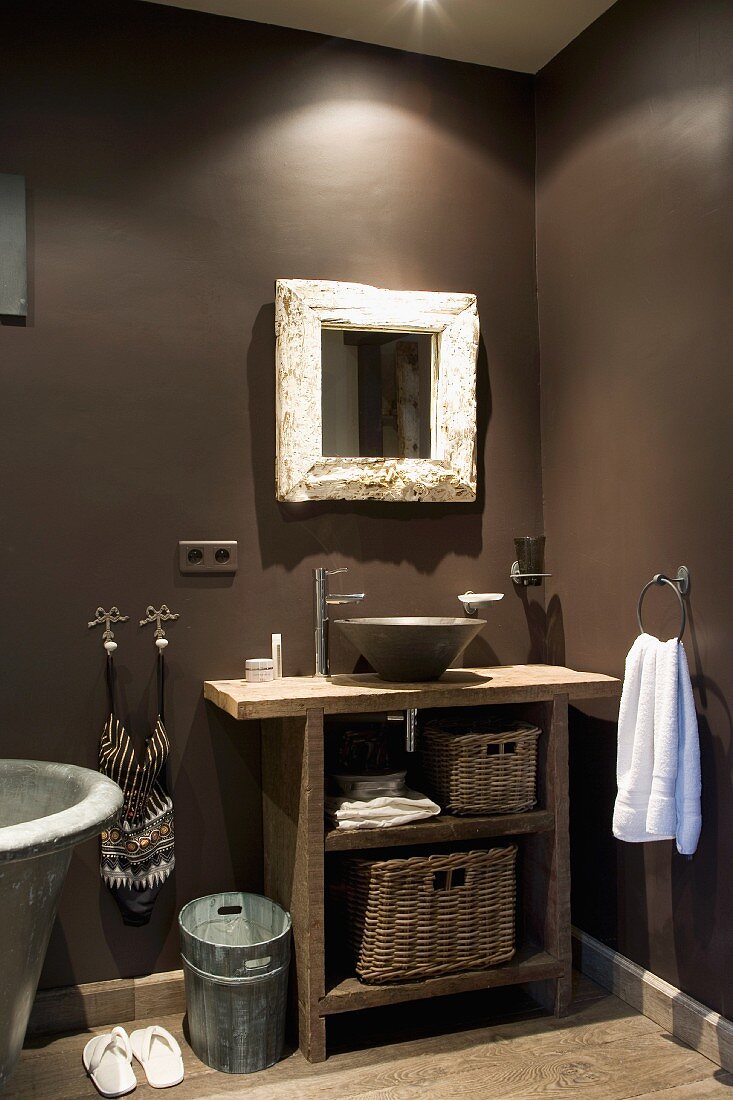 Rustic washstand with countertop ceramic basin and designer tap fitting below mirror in corner of bathroom with walls painted dark grey