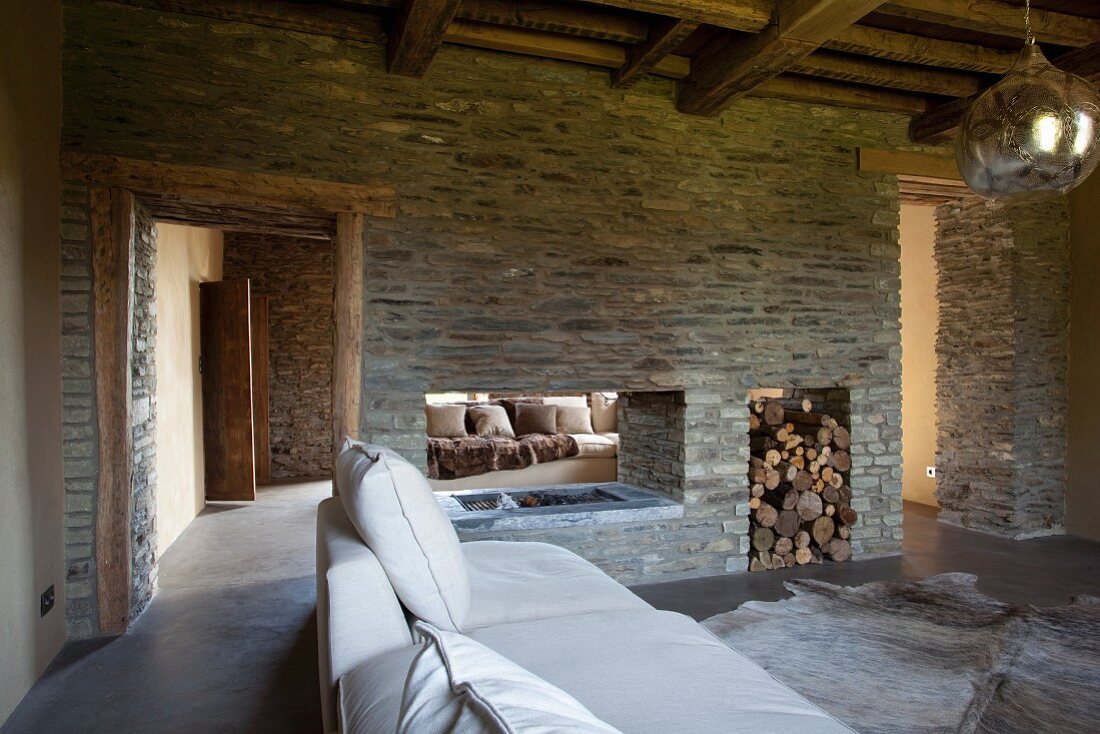 Modern interior with rustic wood-beamed ceiling and stone partition wall with double-sided fireplace and firewood storage