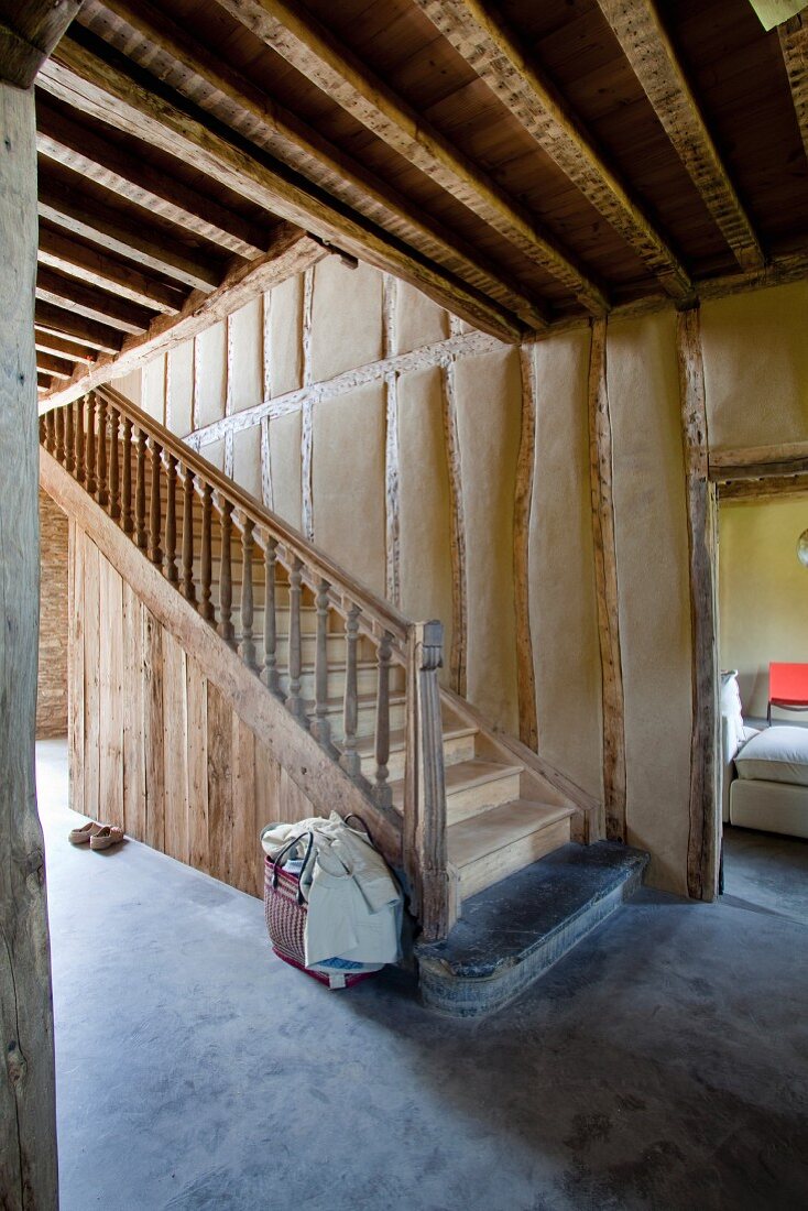 Flur eines Wohnhauses mit sichtbarer Fachwerkkonstruktion, Holzbalkendecke und alter Holztreppe auf glattem Betonboden