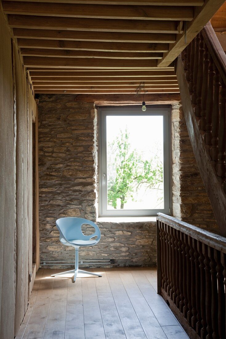 Sonniger Platz für einen hellblauen Drehsessel vor der Natursteinwand im Treppenflur eines Landhauses