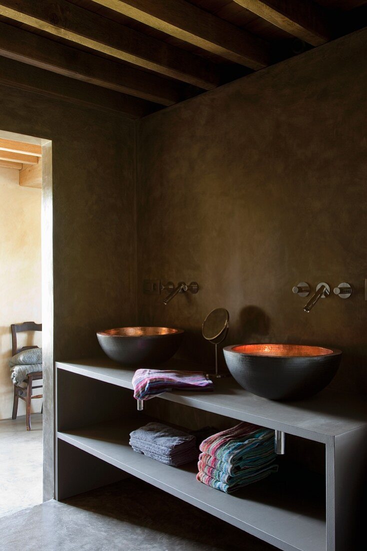 Mixture of styles in bathroom with galvanised washbasins and modern tap fittings on rustic, mud-coloured wall