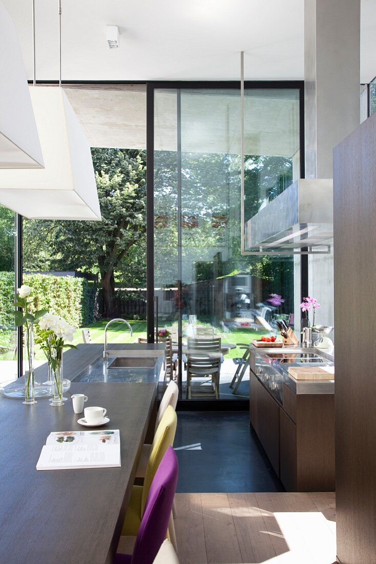 Open-plan, designer kitchen in front of open terrace door with view of garden