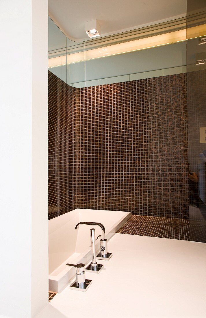 Designer bathroom with rounded corner; sunken bathtub against half-height wall with iridescent, brown mosaic tiles