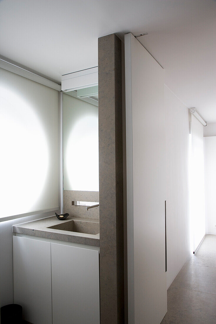 Narrow, modern bathroom with concrete washbasin and white blinds