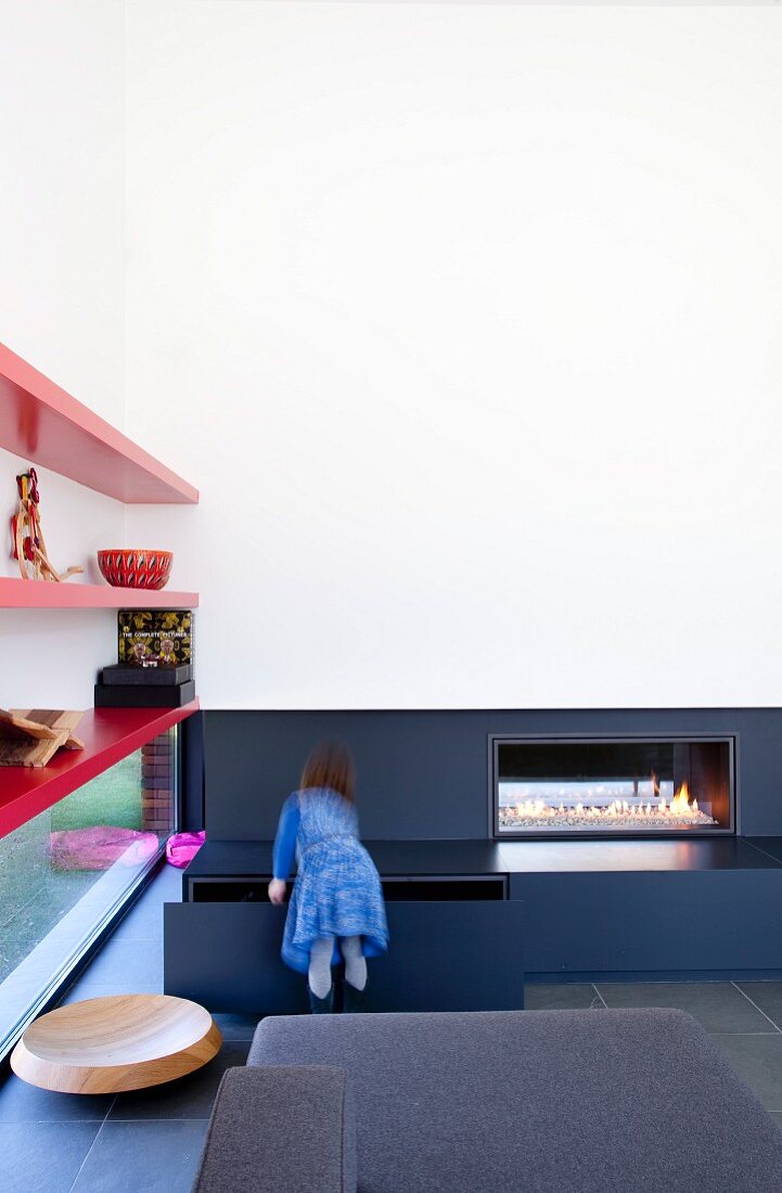 Living room with modern fireplace and red floating shelves over ribbon window