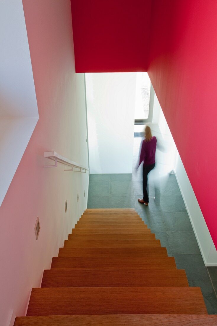 View down staircase with red wall to hallway with stone floor