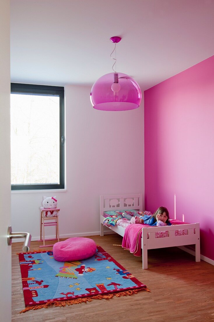 Pink wall in child's bedroom with nursery rug and pink hemisphere lamp