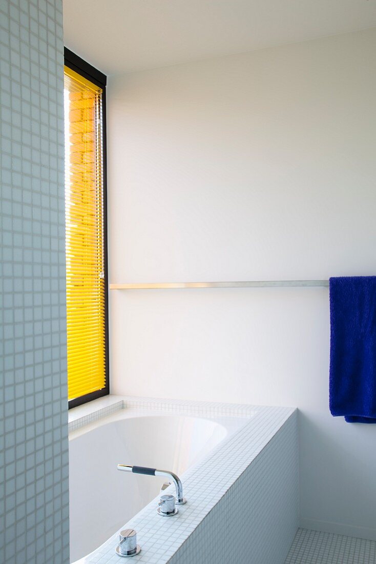 Bathtub in bathroom with mosaic tiles and yellow louver blind