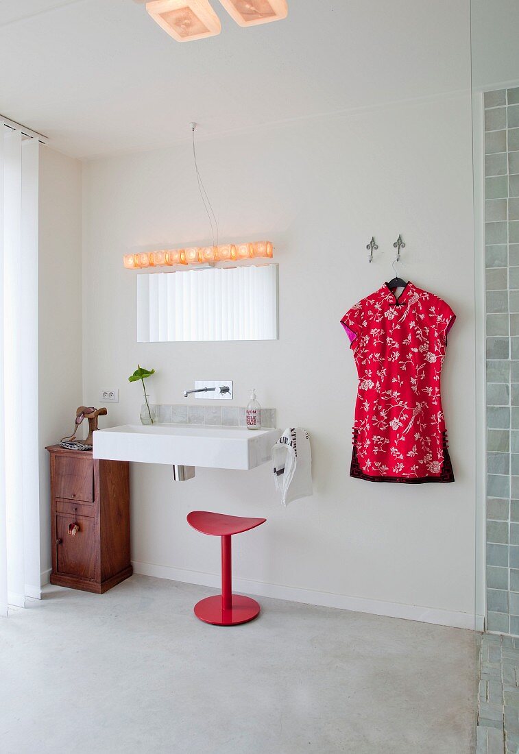 Simple bathroom with modern sink, red stool and dress hung on wall hook